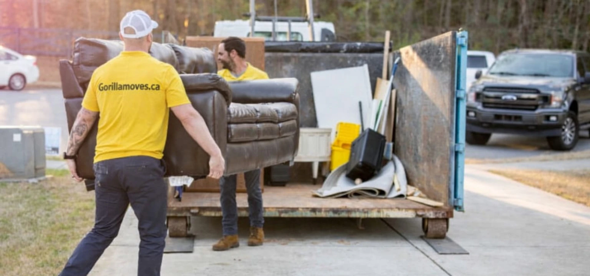 Two Gorilla Moves crew members in yellow shirts loading a sofa into a junk removal bin in Fraser Valley BC